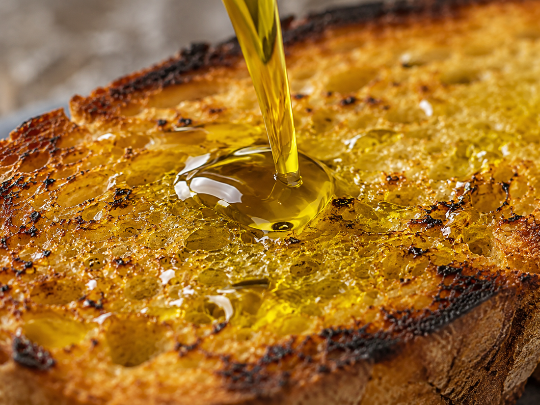 Olio extravergine di oliva italiano 100% appena spremuto versato su bruschetta di pane rustico del Sud Italia tostato